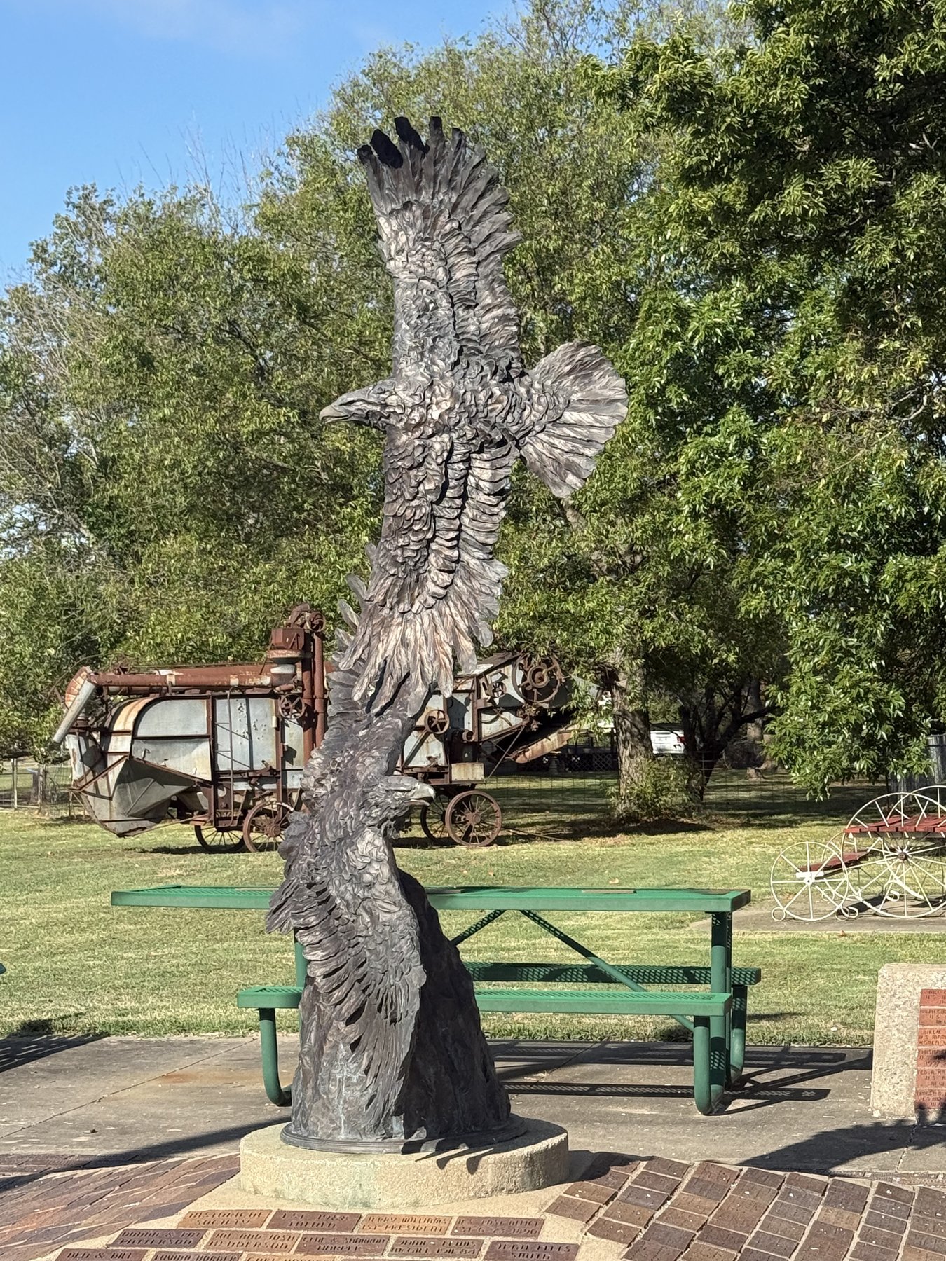 Eagle sculpture beside a picnic table, with vintage farm equipment on the grounds