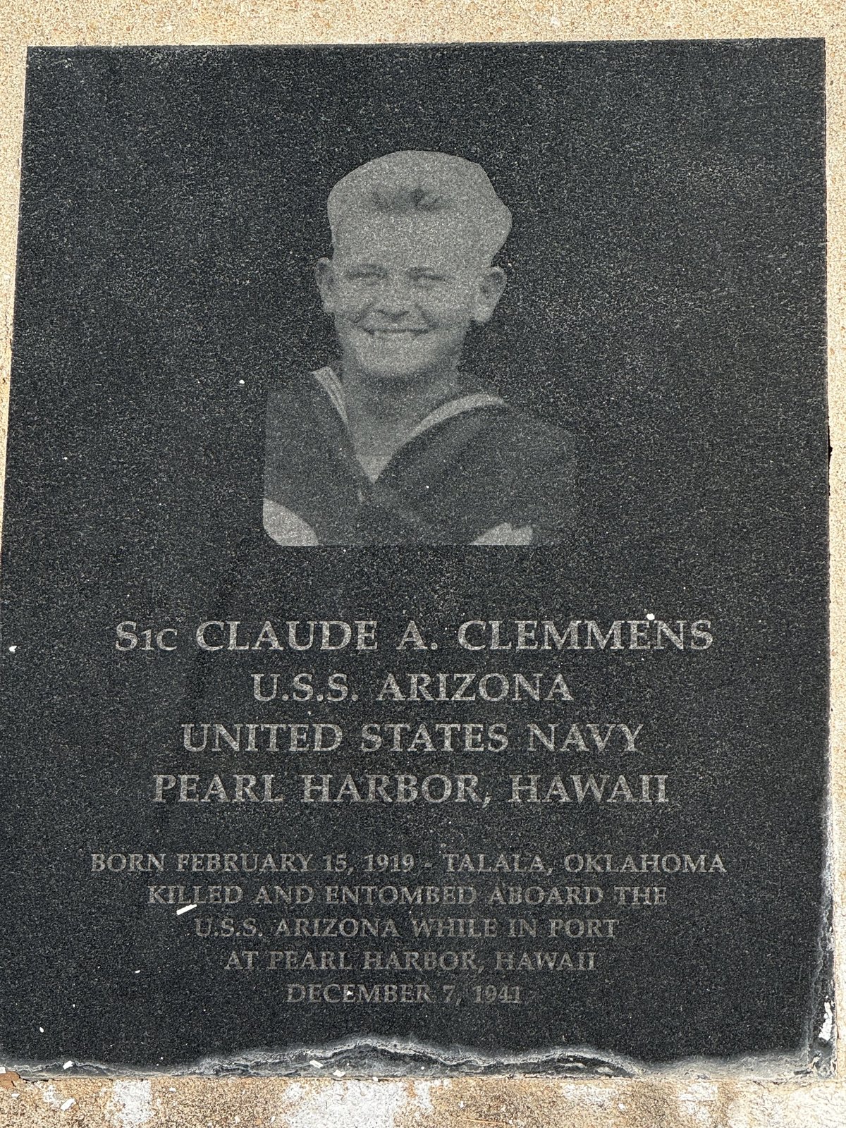 Granite memorial plaque with an etched portrait of S1c Claude A. Clemmens in Navy uniform
