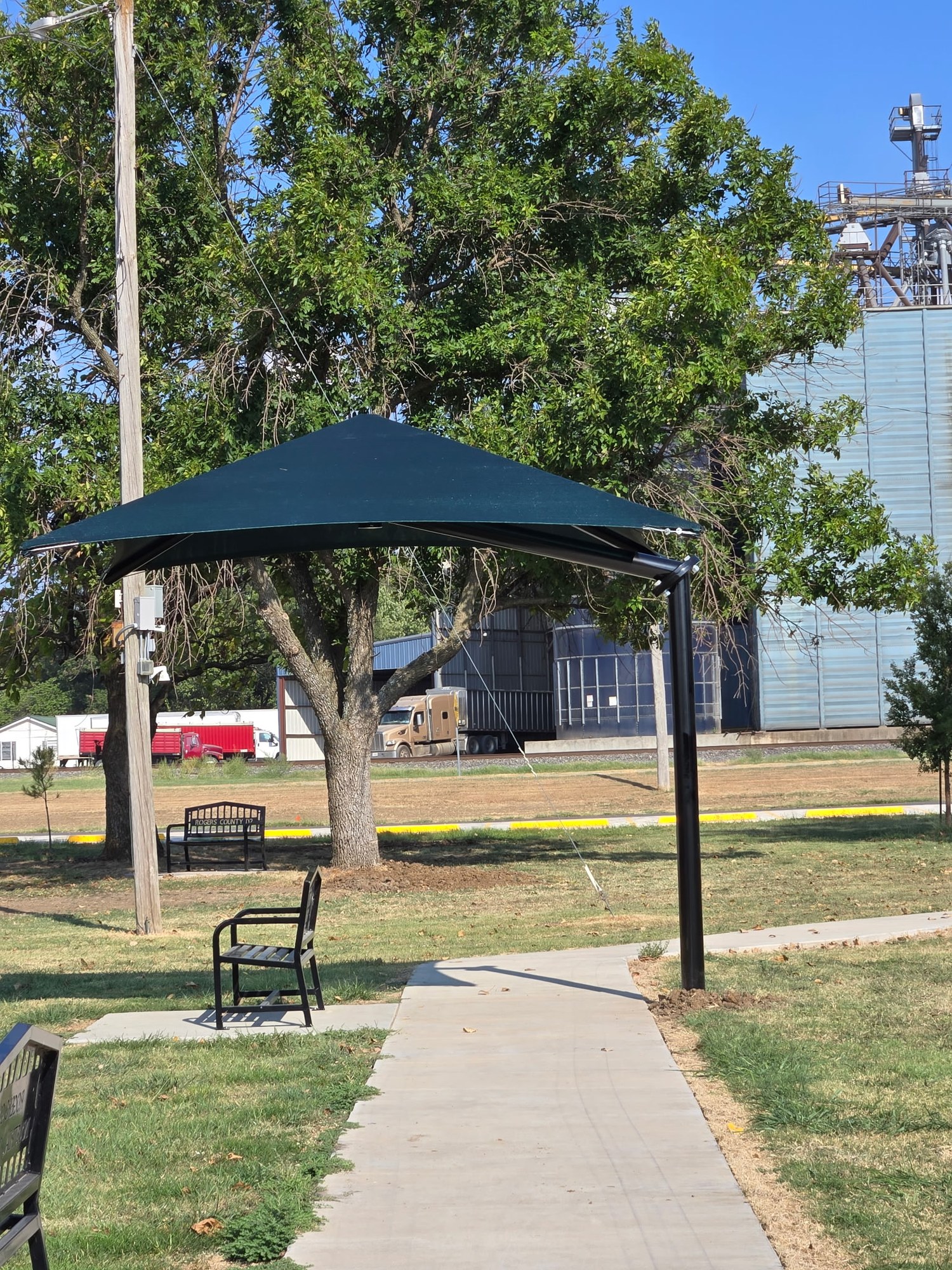 Triangular shade canopy over a walkway and park bench
