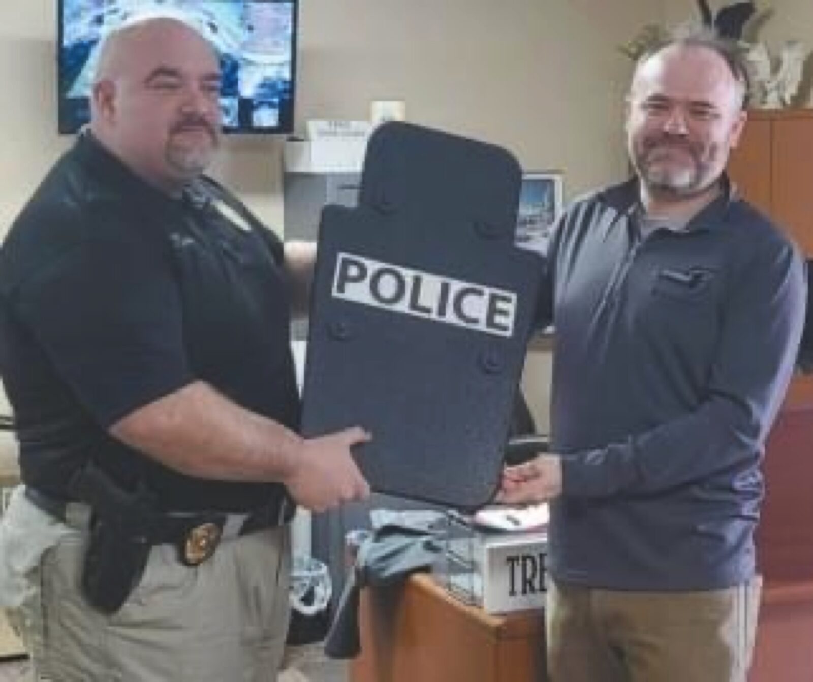 Chief Eaton and a community partner holding a black POLICE ballistic shield in an office on the day the Shield was donated